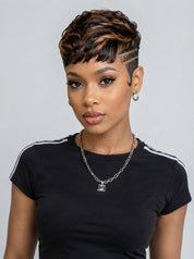 A woman modeling a short, textured wig with dark brown and warm blonde highlights, styled with a side-swept fringe and undercut sides. She is wearing a black t-shirt with white shoulder stripes and a silver chain necklace against a plain light gray background.