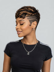 A woman with a short, textured pixie cut featuring dark brown and warm blonde highlights, styled with a sharp side undercut. She is wearing a black t-shirt with white shoulder stripes and a silver chain necklace, set against a solid light gray background.