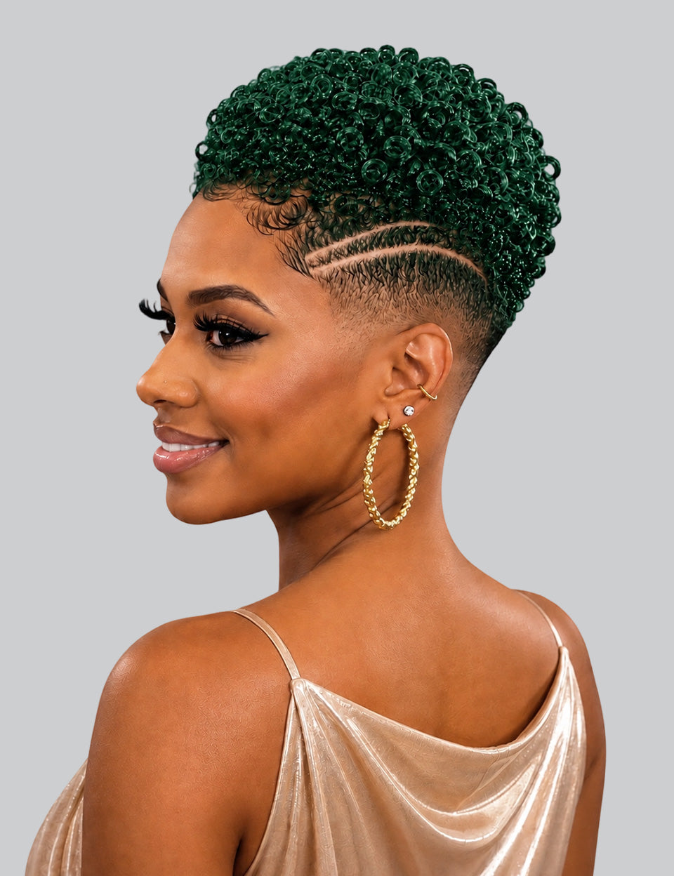 A woman shown in profile with a short, tightly curled hairstyle in deep emerald green and a faded undercut. She is wearing large gold hoop earrings and a champagne satin top against a plain light gray studio background.