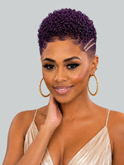 A woman with a short, tightly curled purple wig and gold hoop earrings, wearing a champagne-colored pleated top against a solid gray background.