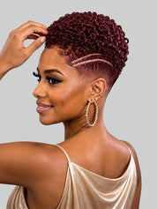 A woman with a short, curly, deep burgundy wig is shown in profile against a solid gray background. She is wearing a champagne-colored satin top and large gold hoop earrings.