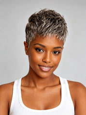 A woman with a short, textured pixie cut featuring ash brown and silver highlights, wearing a white tank top against a solid gray background.