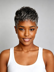 A woman with a short, textured pixie cut featuring dark brown and silver-gray highlights, wearing a white ribbed tank top against a solid gray studio background.