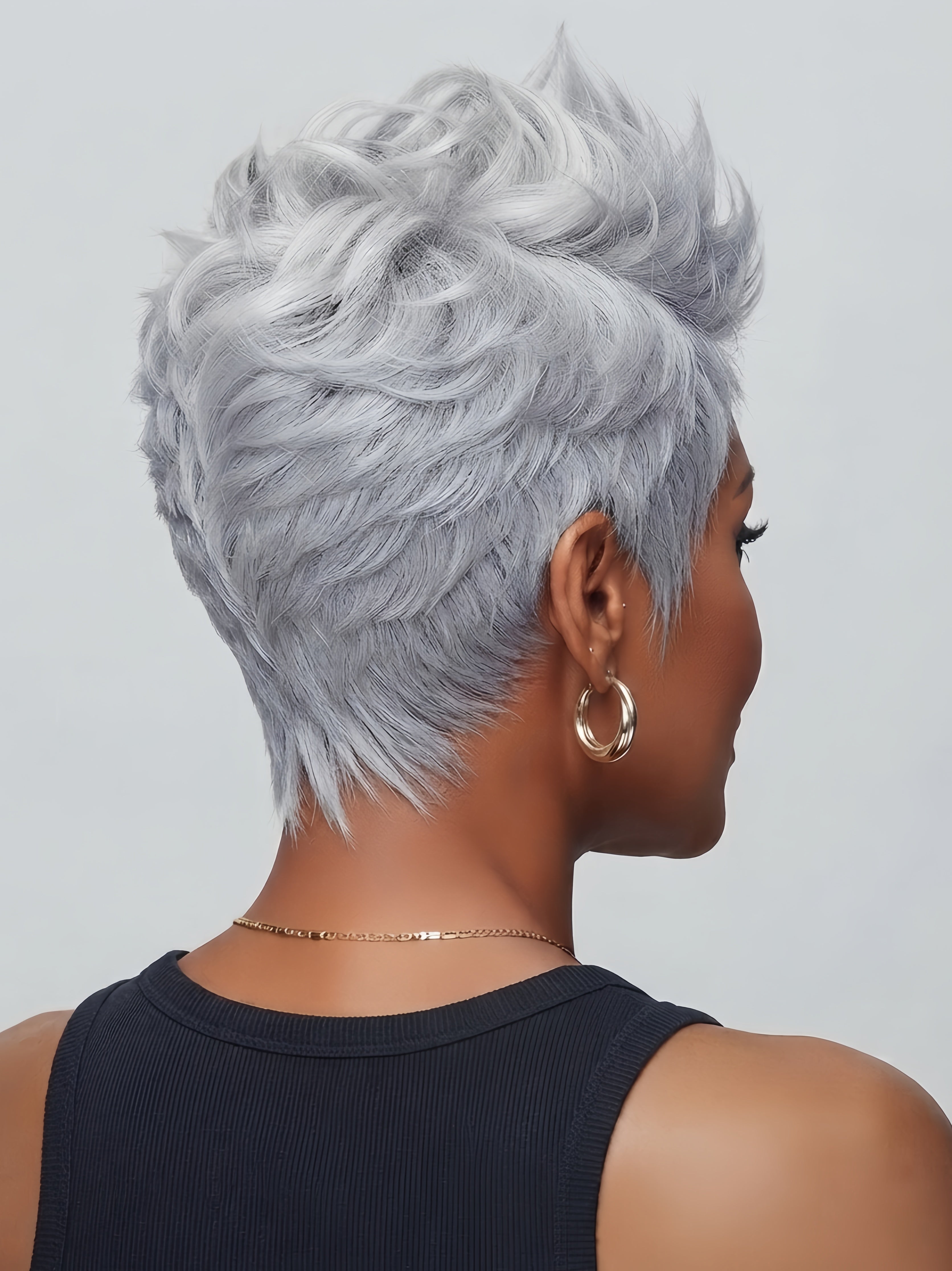 Back view of a short salt and pepper pixie wig showing layered texture and tapered nape. The 100% human hair features a mix of gray and white tones with a natural, fluffy finish.