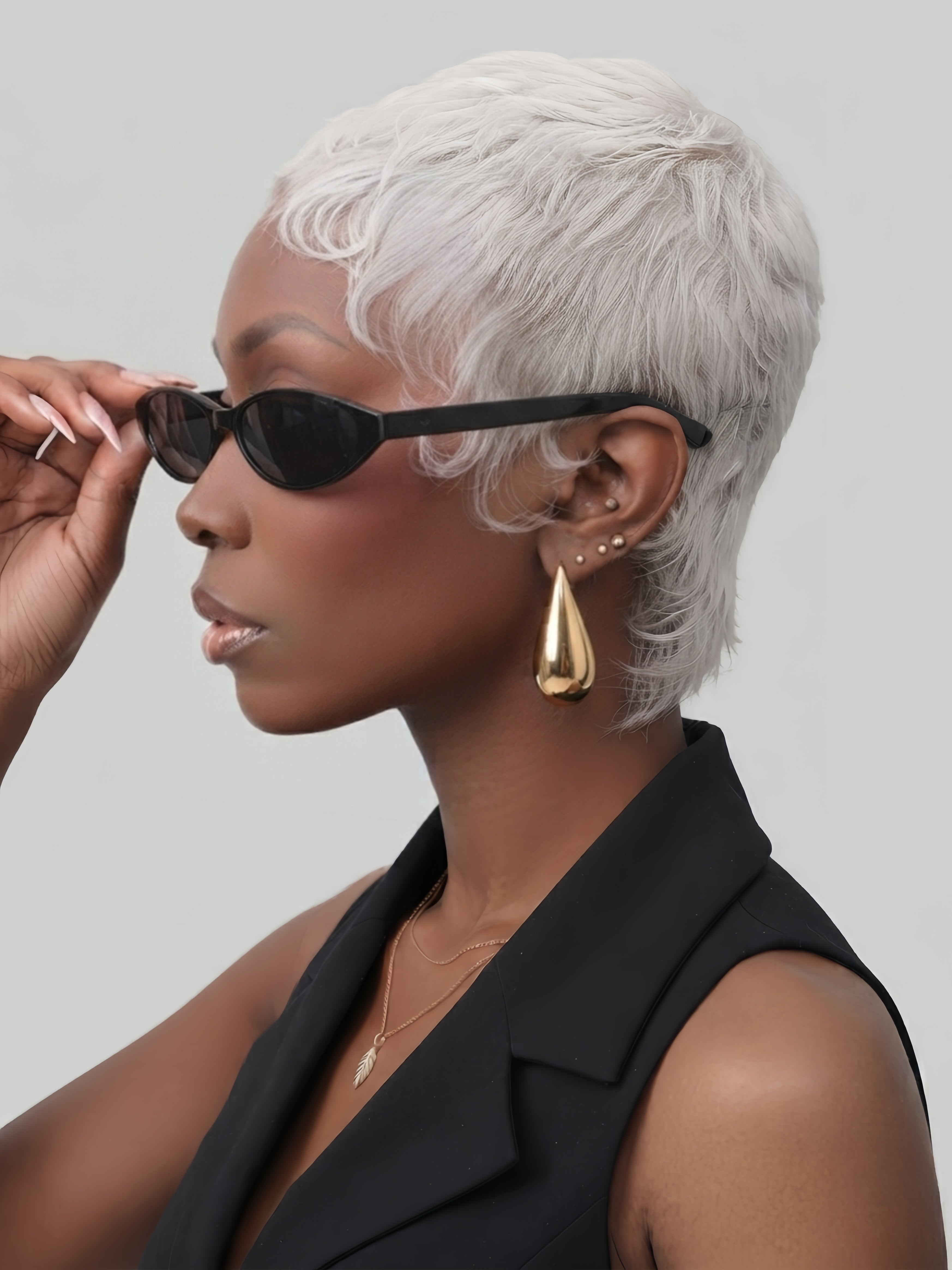 Woman wearing 18K gold-plated stainless steel water drop earrings with high polish finish. The minimalist teardrop design complements her short ICE SILVER pixie wig and chic black sleeveless top, perfect for modern fashion styling.