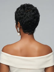 Back view of a woman wearing a short curly pixie wig in black with subtle grey highlights. The image highlights the tapered nape and the dense curl pattern at the crown, complemented by elegant pearl drop earrings and an off-shoulder white dress.