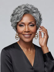 Smiling woman in a grey ombre short wig, featuring a fluffy crown and side-swept bangs. The hairstyle combines a textured top with soft curls around the jawline, creating a polished and confident look ideal for professional or social settings.
