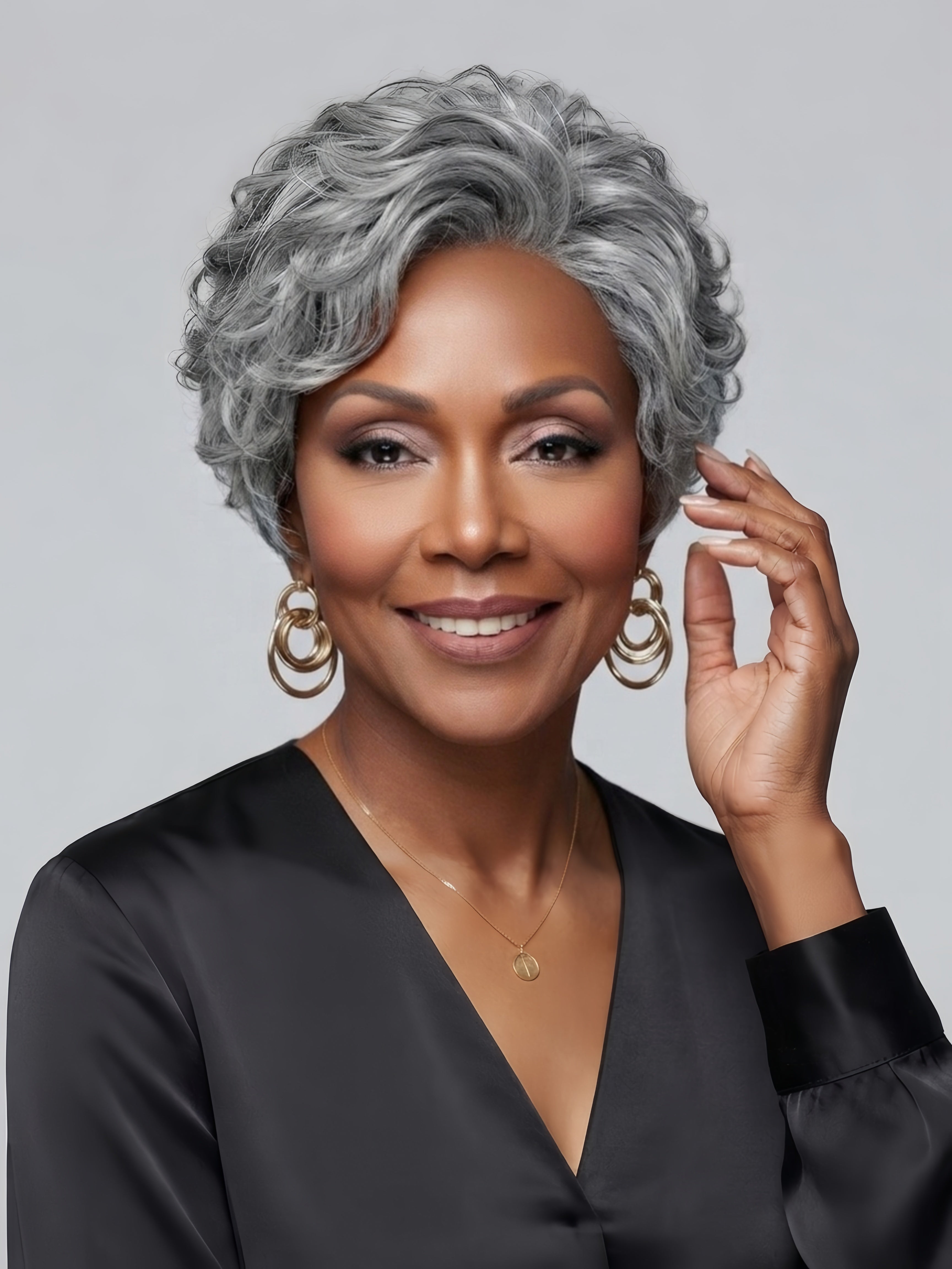 Smiling woman in a grey ombre short wig, featuring a fluffy crown and side-swept bangs. The hairstyle combines a textured top with soft curls around the jawline, creating a polished and confident look ideal for professional or social settings.
