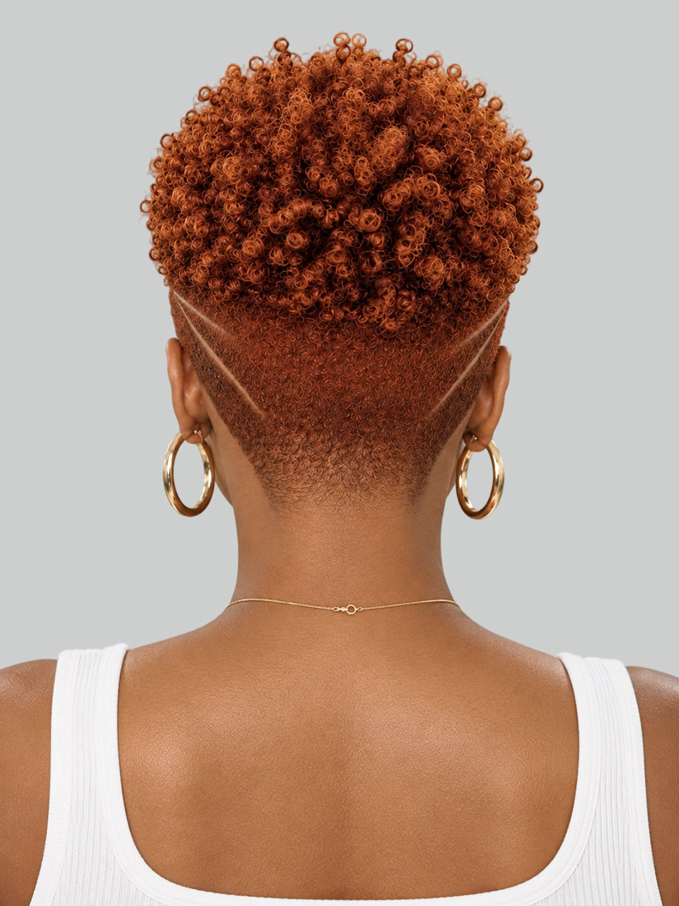Back view of a person with a short, textured, curly hairstyle in a warm coppery brown color, styled with a geometric fade on the sides. The person is wearing large gold hoop earrings and a delicate gold necklace, set against a solid light gray background.