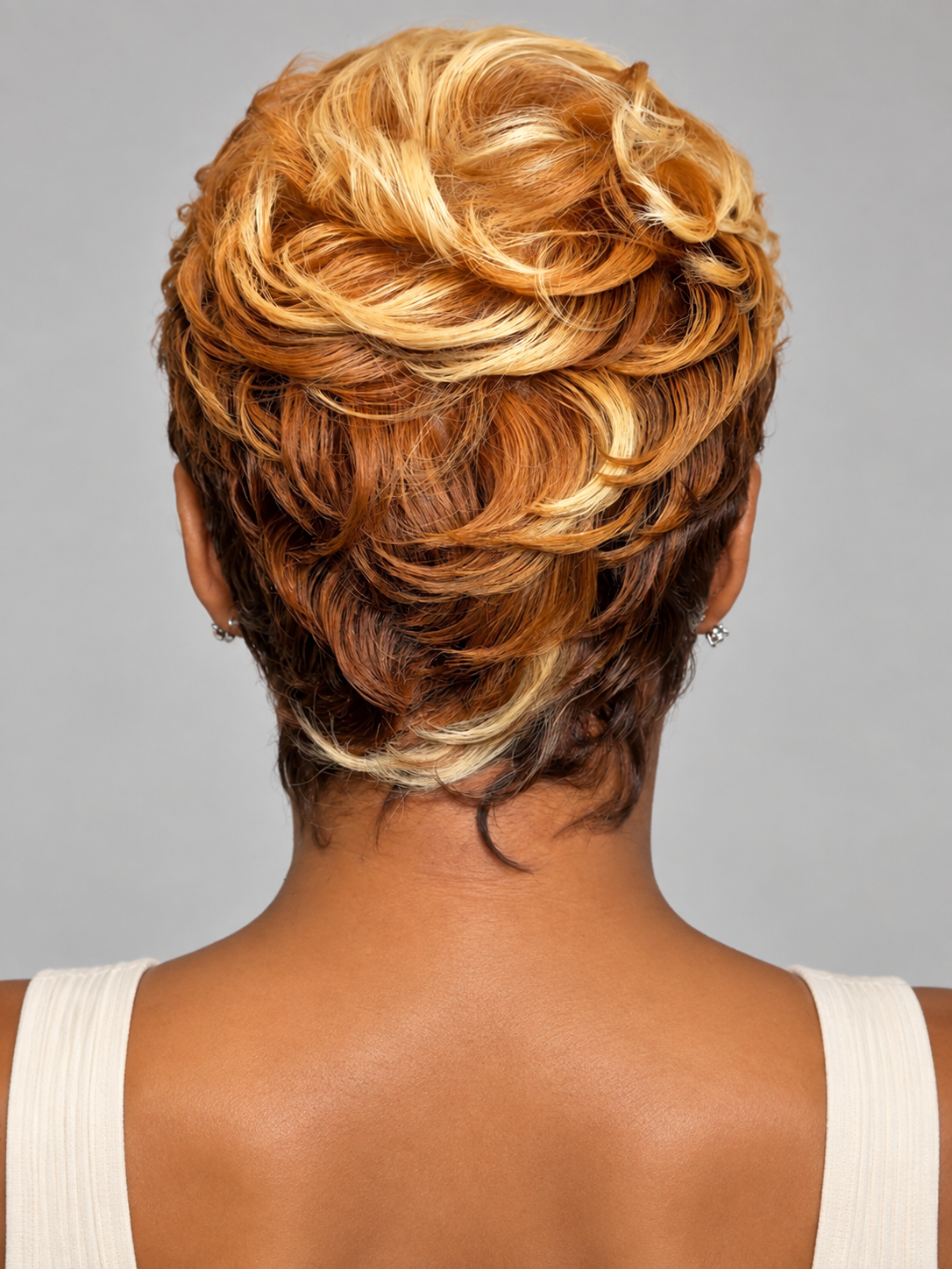 Back view of a person wearing a short textured hairstyle with layered golden blonde, caramel brown, and dark brown tones against a plain gray background.
