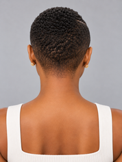 Back view of a person with short, textured black hair wearing a white ribbed tank top and small gold stud earrings against a plain gray background.