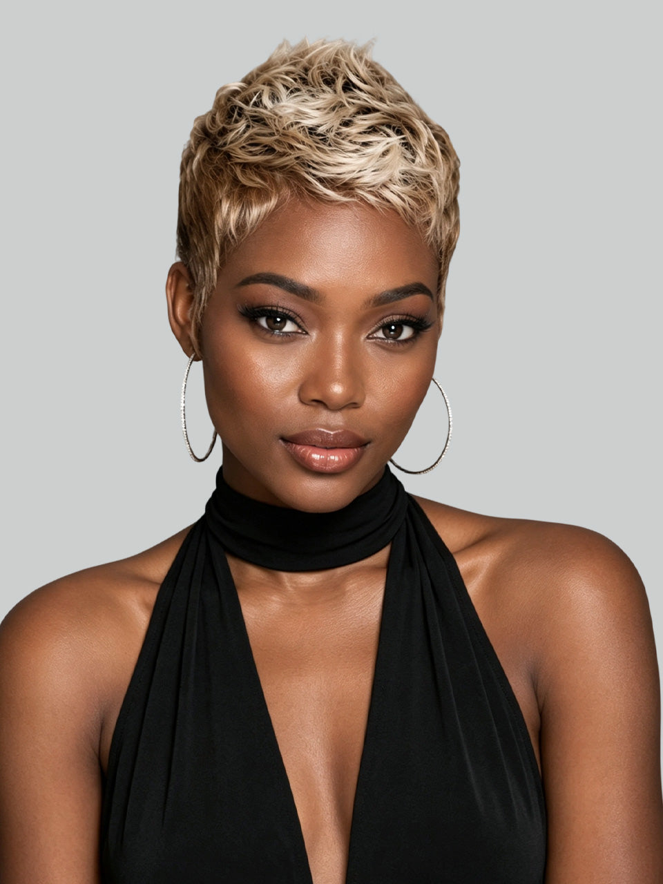 Front view of a woman wearing a short blonde pixie cut wig made of 100% human hair. The wig features a natural parting and textured layers, paired with large hoop earrings and a black halter top.