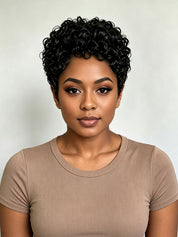 A woman with short, curly black hair wearing a beige short-sleeve ribbed t-shirt, photographed against a neutral light gray background.