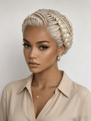 A woman with platinum blonde hair styled in an intricate braided updo, wearing a beige collared blouse and delicate jewelry against a light gray background.