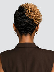 Back view of a person wearing a short, styled hairpiece or wig with dark black textured hair on the lower half and warm golden-blonde curly hair on the upper half, paired with a dark brown sleeveless top against a light gray background.