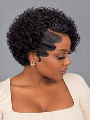 A woman with a short, curly black wig shown in profile against a plain gray studio background. The wig has defined waves and a clear side part, and she is wearing a cream ribbed top and a small gold earring.