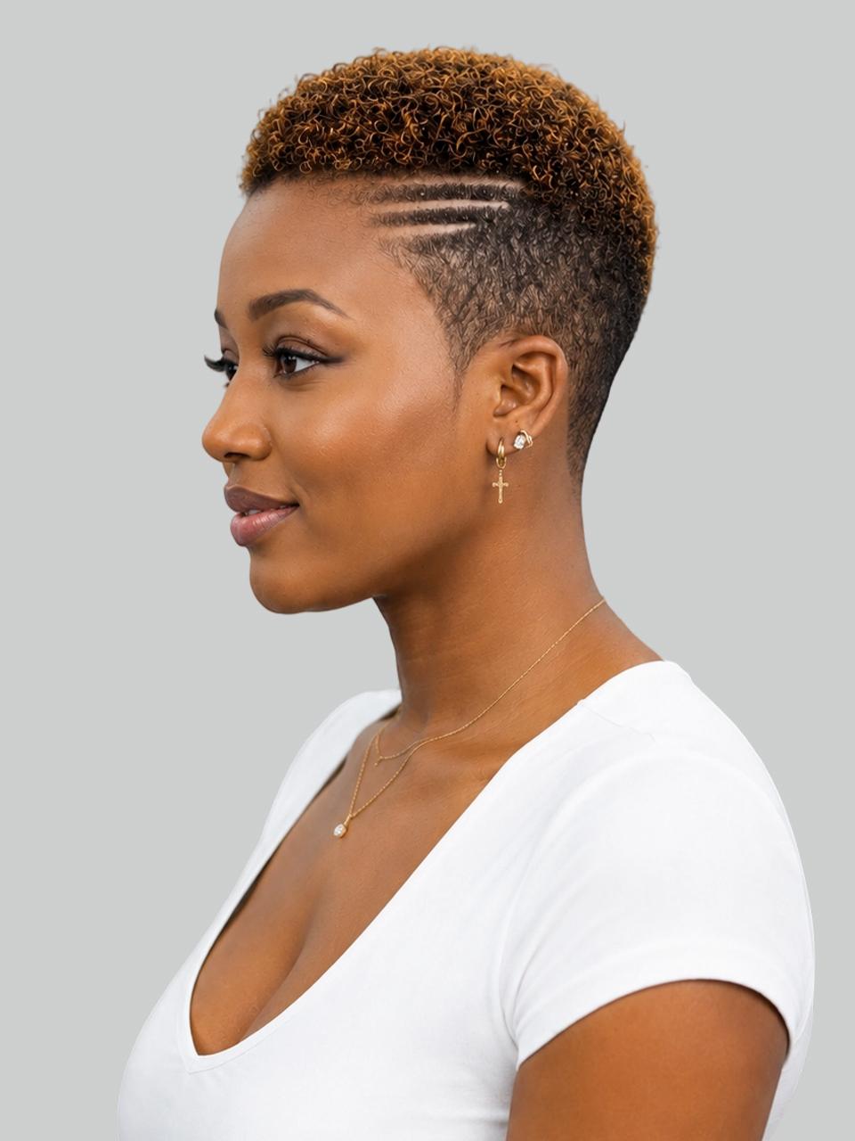 A woman in profile wearing a white v-neck top, gold necklace, and gold cross earring, showcasing a short textured hairstyle with geometric side-swept lines against a solid gray background.