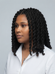 A woman with long, tight, black twisted braids or box braids wearing a white collared shirt, shown in a three-quarter profile against a light gray background.