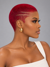 A close-up side profile of a woman with a vibrant red, micro-textured pixie cut and geometric side designs, wearing gold hoop earrings and a white strap top against a solid gray background.