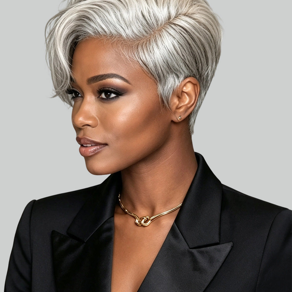 A woman with a short, layered silver-gray pixie cut hairstyle, wearing a black satin blazer and a gold chain necklace, shown in a three-quarter profile against a solid gray background.