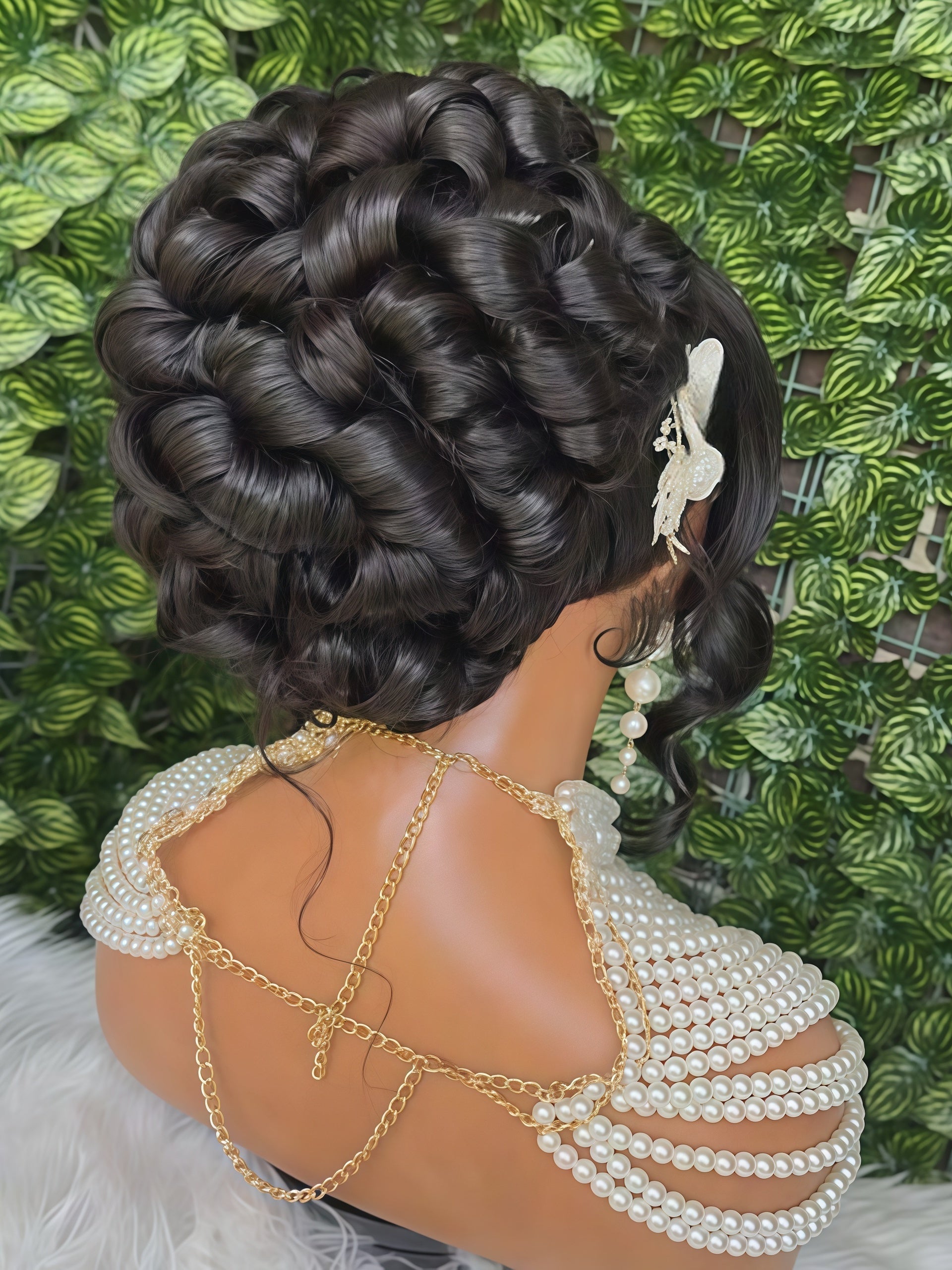 A mannequin bust with an elaborate updo hairstyle, shown from the back. The hair is dark brown with soft waves and is styled with a white hair accessory.