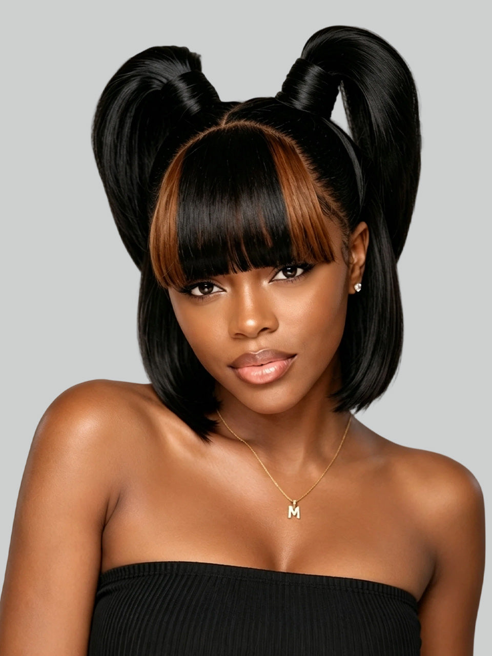 A woman with a black bob haircut, straight-cut bangs, and two high pigtails styled with warm brown highlights, wearing a black strapless top against a light gray background.