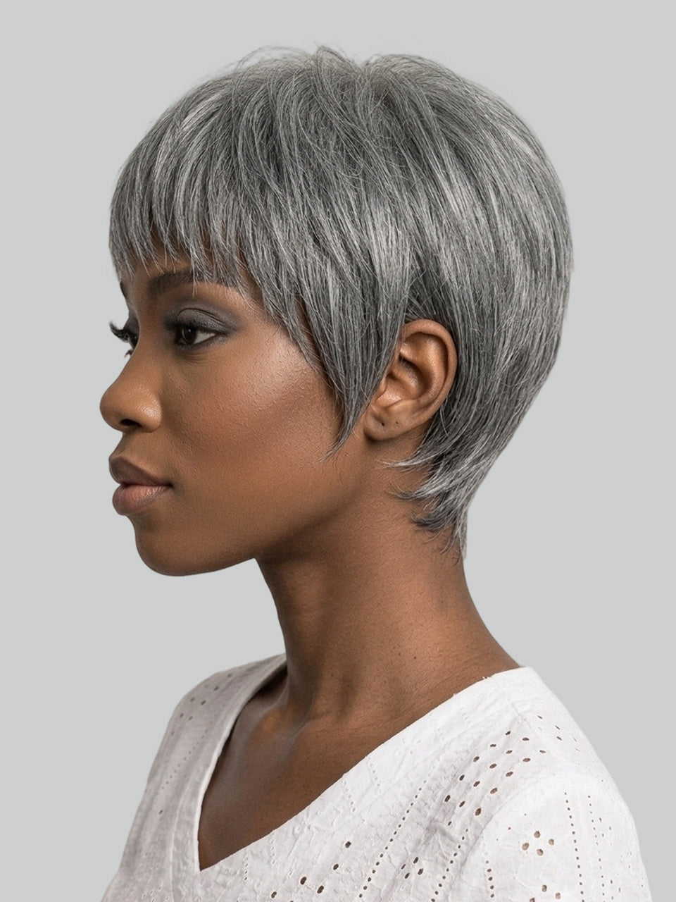 A woman shown in side profile wearing a short, layered gray wig against a plain light gray background.