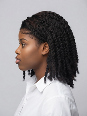 A woman in profile wearing a white collared shirt, showcasing a black curly hair extension or wig with defined root lines and small front bangs, set against a solid light gray background.