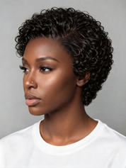 A woman with a short, curly black wig or hairpiece shown in profile against a plain light gray background. The hair is tightly curled and styled in a pixie cut, with a white crew-neck top visible below.
