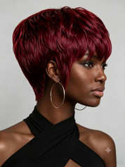 A woman in profile wearing a short, layered pixie wig with deep burgundy-red hair, styled with a side-swept bang and voluminous texture. She is wearing large gold hoop earrings and a black halter top against a neutral gray background.
