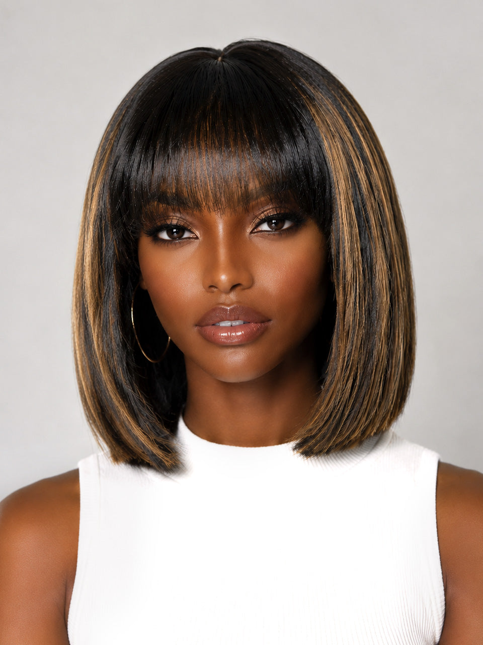 A woman wearing a straight, shoulder-length bob wig with bangs. The wig has a dark brown to black base with warm caramel and light brown highlights, styled against a neutral gray background.