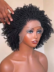 A close-up of a black curly wig with a lace front, displayed on a mannequin head. A hand is adjusting the hair on top, and a clear lace front overlay is visible near the forehead.