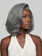 A woman wearing a short, layered gray wig with subtle silver highlights, styled in a bob length with soft waves. She is wearing a white halter top against a solid light gray background.