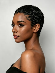 A woman wearing a short, voluminous curly wig in black, styled with a high puff on top, paired with a white V-neck t-shirt against a solid gray studio background.