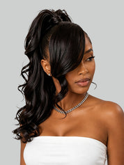 A woman modeling a dark brown half-upside ponytail extension with side-swept bangs and loose curls, paired with a white strapless top against a solid gray background.