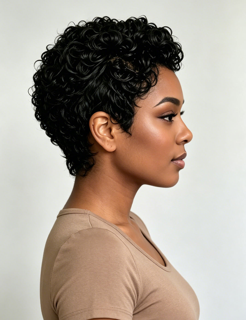 A woman shown in side profile wearing a short, curly black wig against a plain light gray studio background.