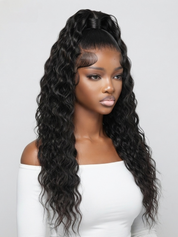 A woman modeling a long, dark brown to black deep wave wig with a high top ponytail and side-swept bangs, wearing a white off-the-shoulder top against a light gray background.