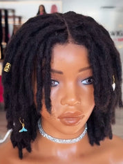 Black dreadlock wig on a mannequin head with a silver rhinestone choker and gold earrings, set against a blurred indoor background.