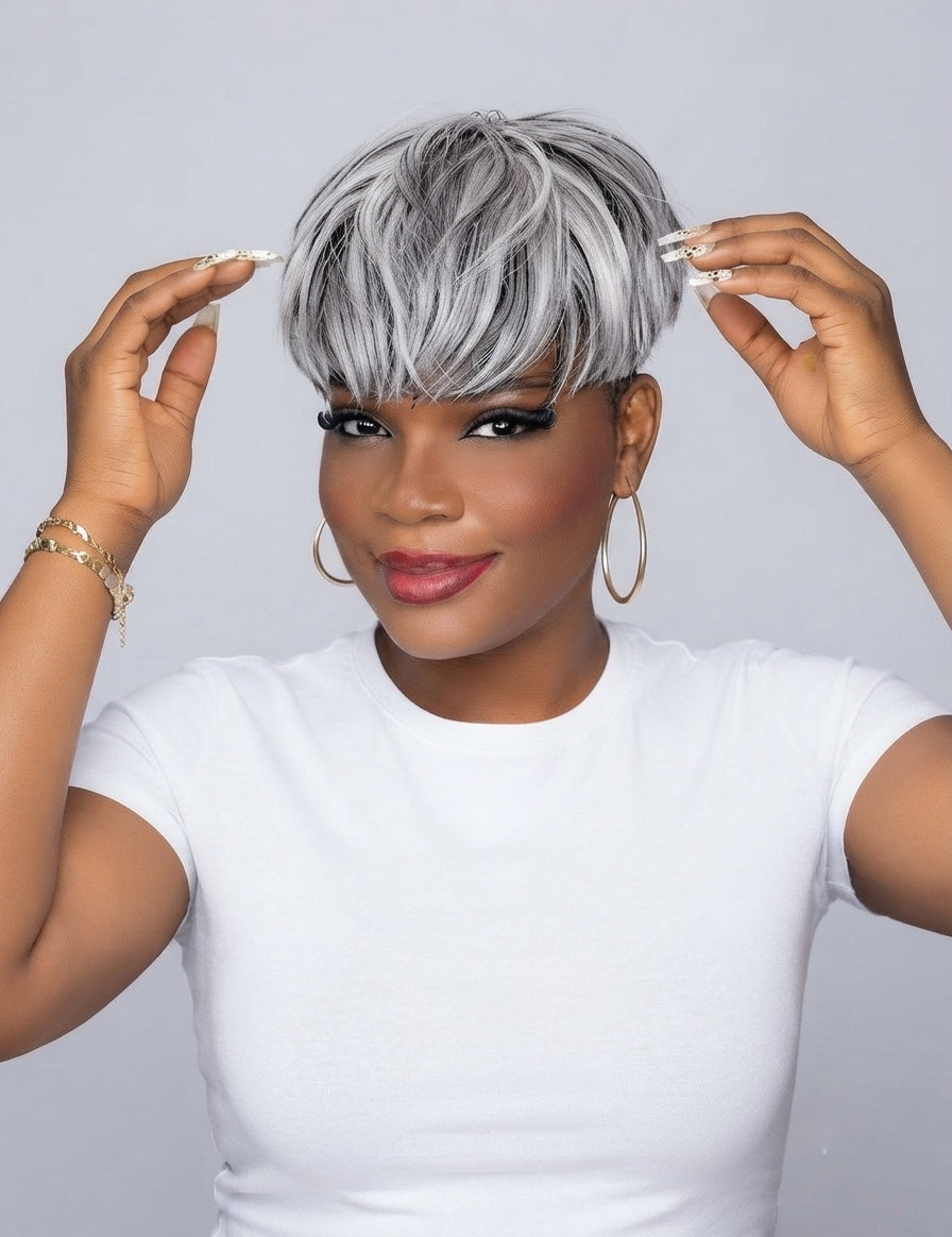 A woman wearing a short, layered silver and gray wig with bangs, posing against a light gray background while adjusting her hair with both hands.