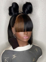 A mannequin head wearing a black wig with a center part, straight bangs, and two high buns, photographed against a light textured wall.