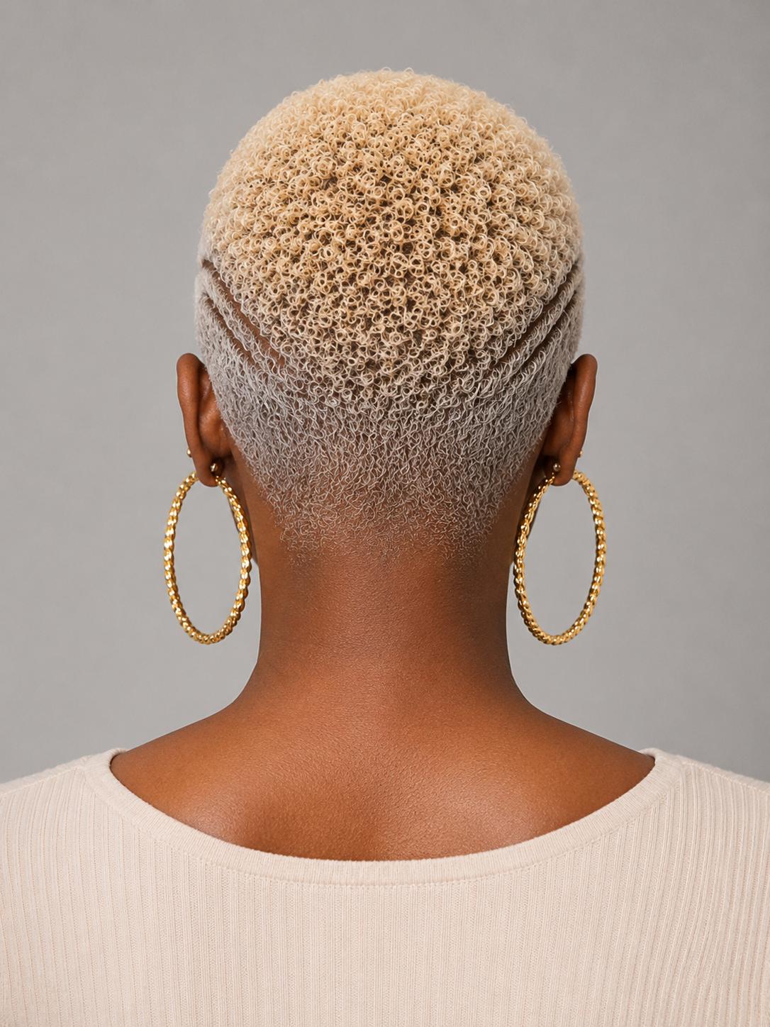 Rear view of a person with a short textured blonde haircut wearing large gold hoop earrings and a cream ribbed top against a plain gray background.