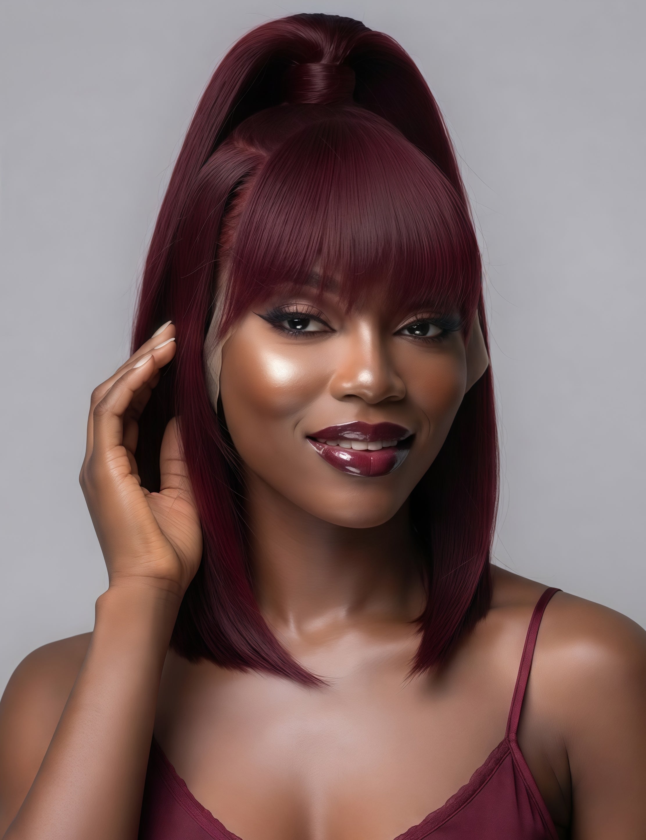 A woman with a dark burgundy high ponytail wig and matching bangs, posing against a solid gray studio background.