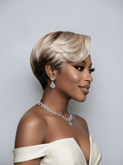 A woman in profile wearing a short, layered wig with a dark brown root and warm blonde highlights, styled with a silver rhinestone necklace and matching drop earrings against a light gray background.