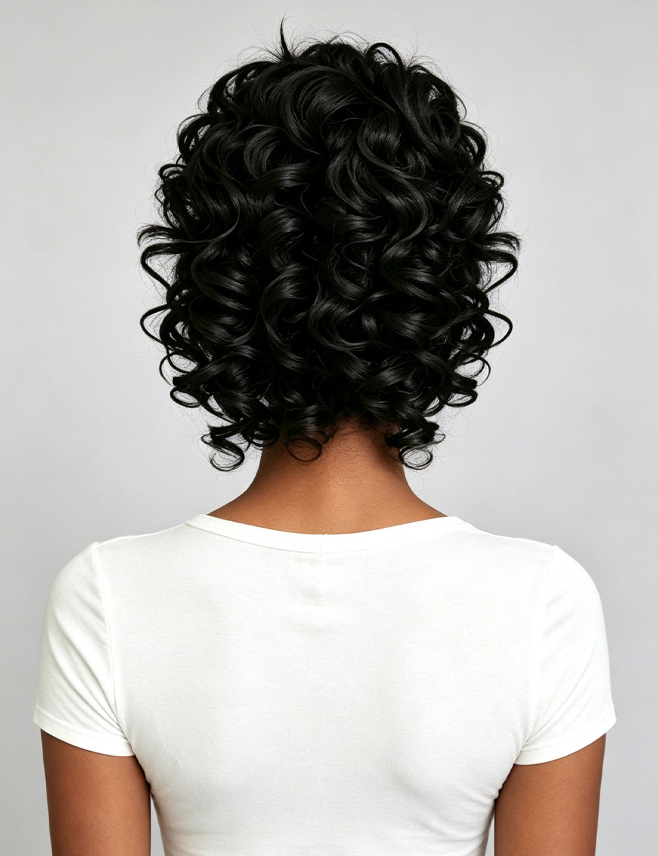 Back view of a person with short, voluminous, tightly curled black hair wearing a white t-shirt against a light gray background.