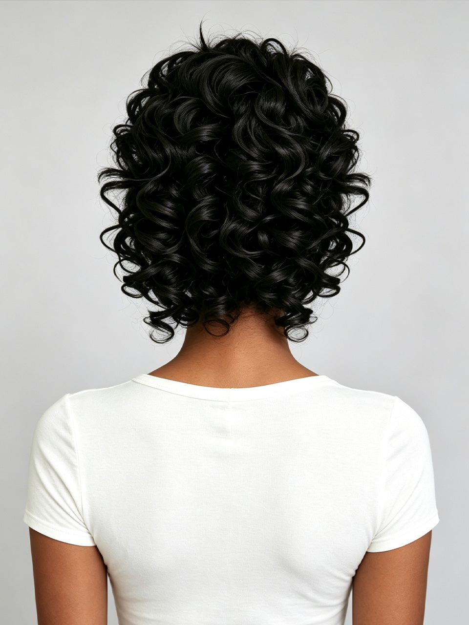 Back view of a person with short, voluminous, tightly curled black hair wearing a white t-shirt against a light gray background.