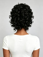 Back view of a person with short, voluminous, tightly curled black hair wearing a white t-shirt against a light gray background.