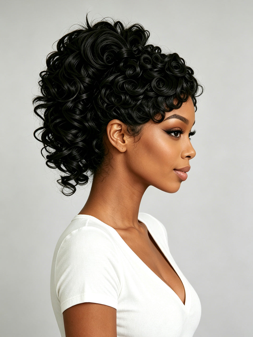 A woman in profile wearing a short, voluminous black curly wig against a light gray studio background.