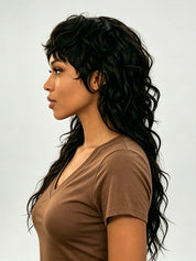 A woman shown in side profile wearing a long, dark brown to black wavy wig with layered bangs and a side-swept look, paired with a brown short-sleeve V-neck top against a light gray studio background.