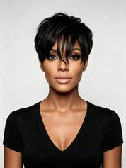 A woman with a short, layered black pixie cut and straightened bangs, wearing a black V-neck top against a light gray studio background.