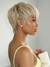 A woman shown in side profile wearing a short, layered blonde wig with a pixie cut, paired with a pale yellow top and a white ribbed sleeve.